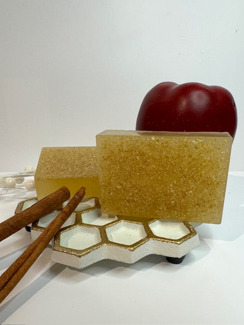 Two bars of soap on a honeycomb stand with an apple and cinnamon sticks on a white background
