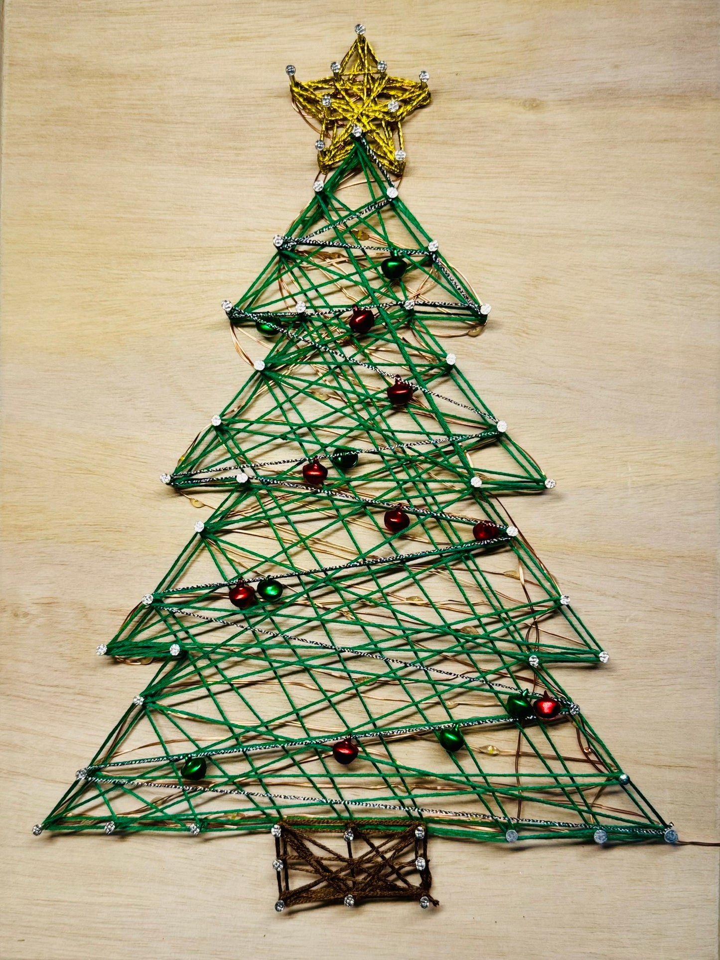 String art Christmas tree on a wooden surface with jingle bell ornaments