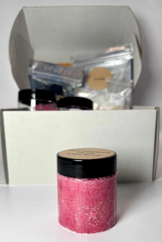 Black Raspberry & Vanilla Sugar Scrub kit with a clear jar of bright pink scrub and a black lid, plus packaged ingredients.
