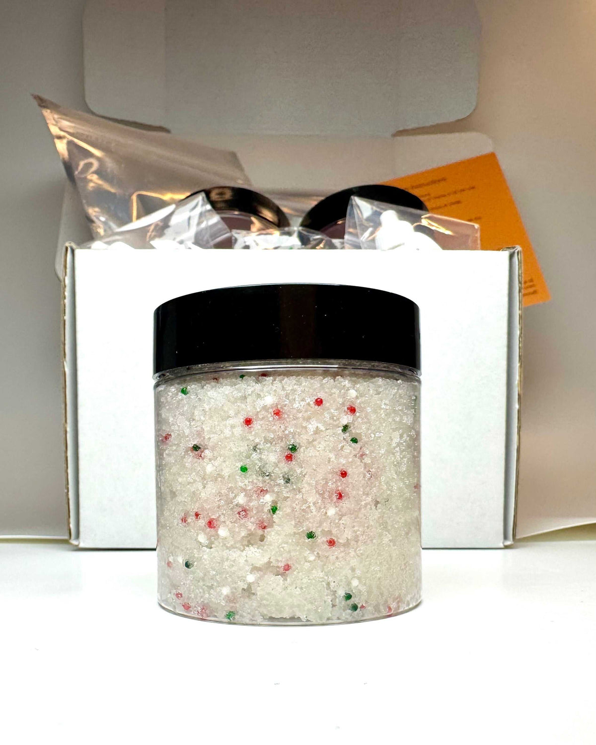 Christmas Sugar Cookie Sugar Scrub in a clear jar with a black lid, white sugar and festive red and green sprinkles
