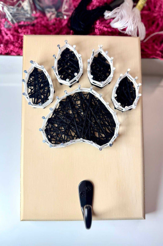Finished black dog paw string art with white border on a wood board with a double hook for hanging a leash